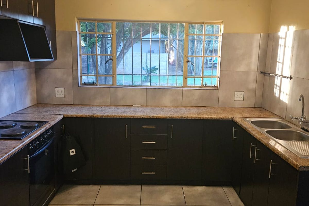 A functional U-shaped kitchen featuring dark cabinetry, laminate countertops, a double basin sink, and built-in oven with hob, overlooking the garden.