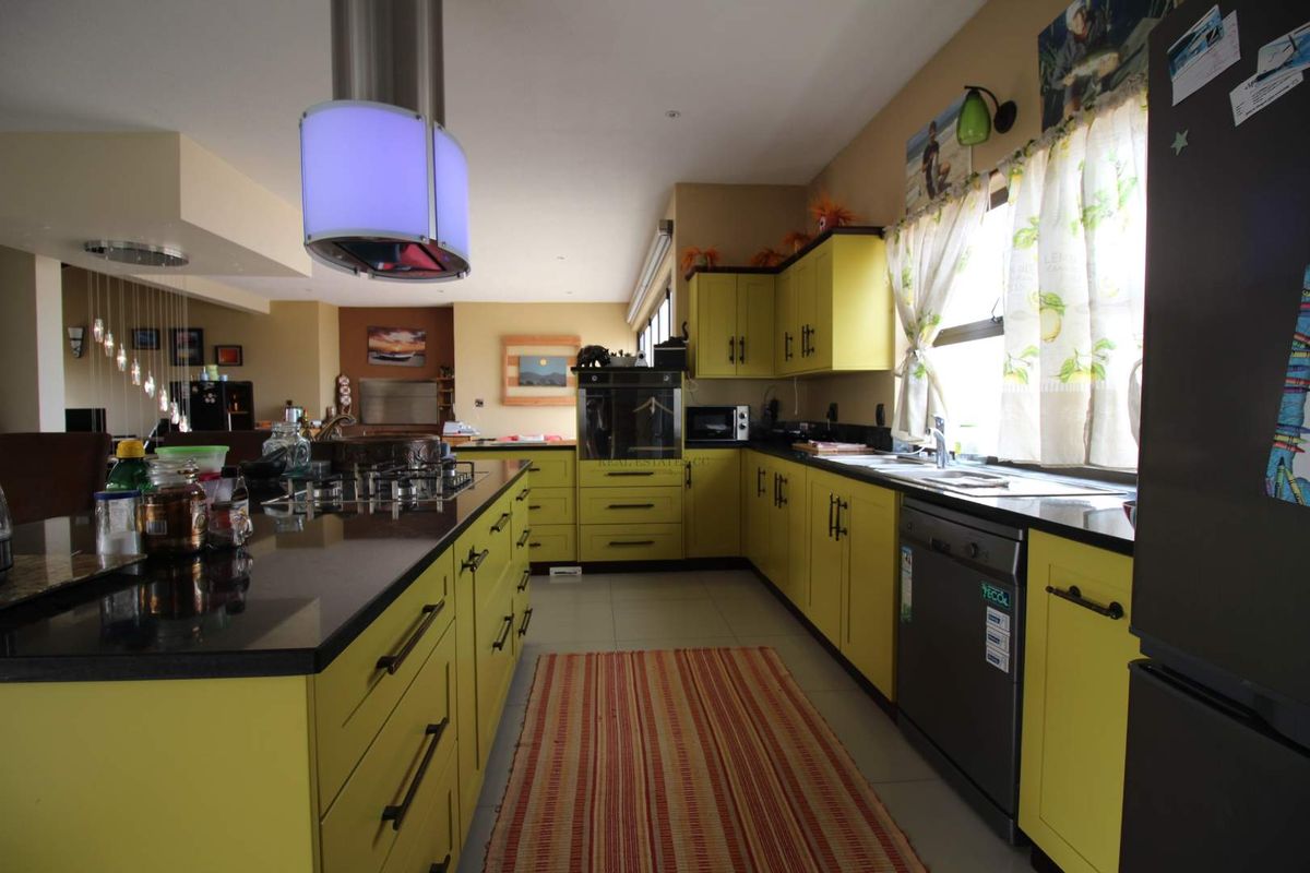 Spacious kitchen featuring vibrant yellow cabinetry, dark granite countertops, a central island with a gas hob, and a modern stainless steel extractor fan.