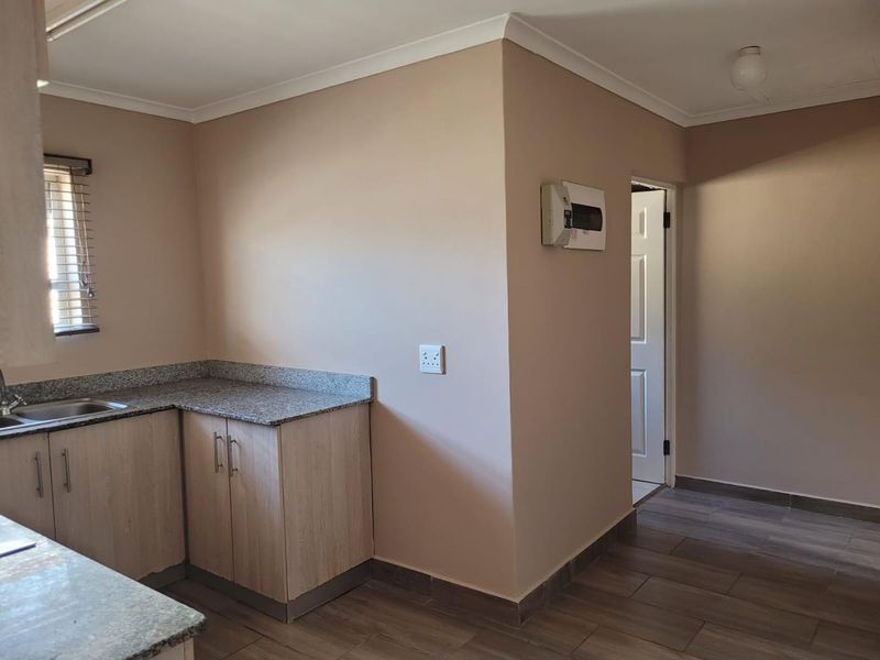 A clean, functional kitchen area featuring granite countertops, light wood-finish cabinetry, and tiled flooring, leading into an adjacent hallway.