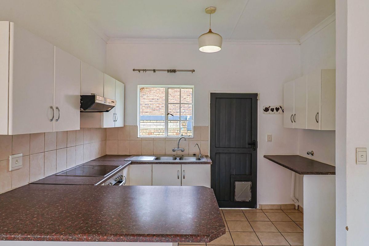 A functional kitchen featuring white cabinetry, dark laminate countertops, a built-in electric hob, extractor fan, and tiled flooring with direct exterior access.