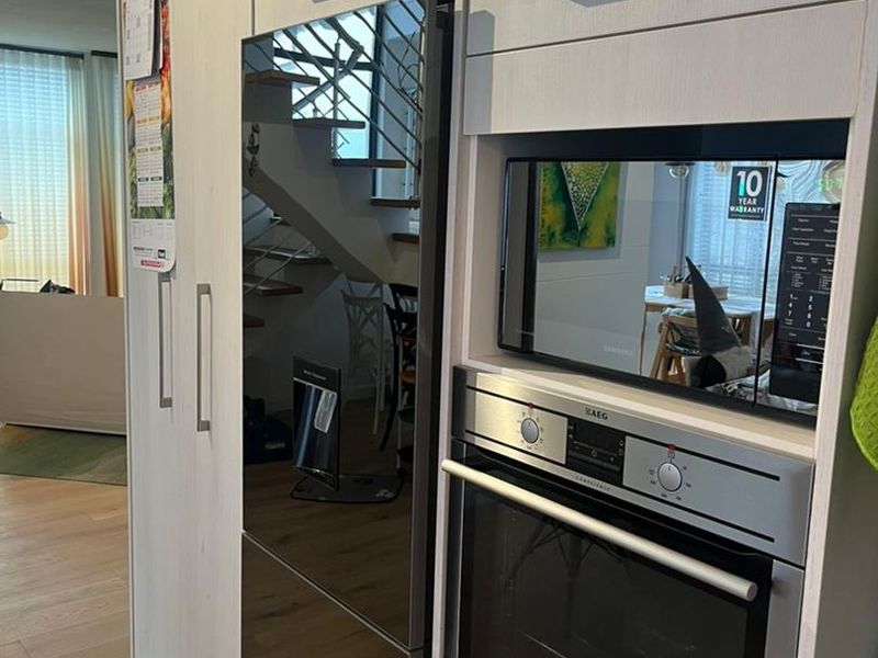 Modern kitchen featuring light wood cabinetry, integrated refrigerator, and built-in AEG oven and microwave, seamlessly flowing into the living area.
