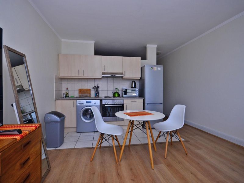 Open-plan living area featuring a compact kitchen with built-in cabinetry, integrated oven, extractor fan, and tiled flooring, seamlessly flowing into the living space.
