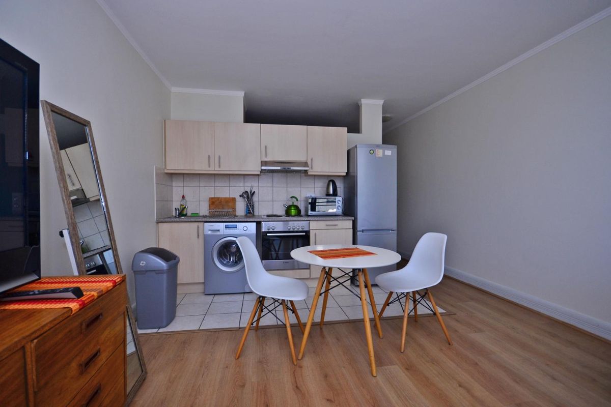 Open-plan living area featuring a compact kitchen with built-in cabinetry, integrated oven, extractor fan, and tiled flooring, seamlessly flowing into the living space.