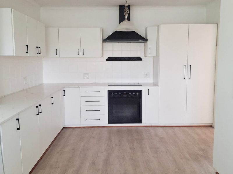 A clean, modern kitchen featuring white cabinetry, integrated appliances, a built-in oven with hob, and light-toned laminate flooring.