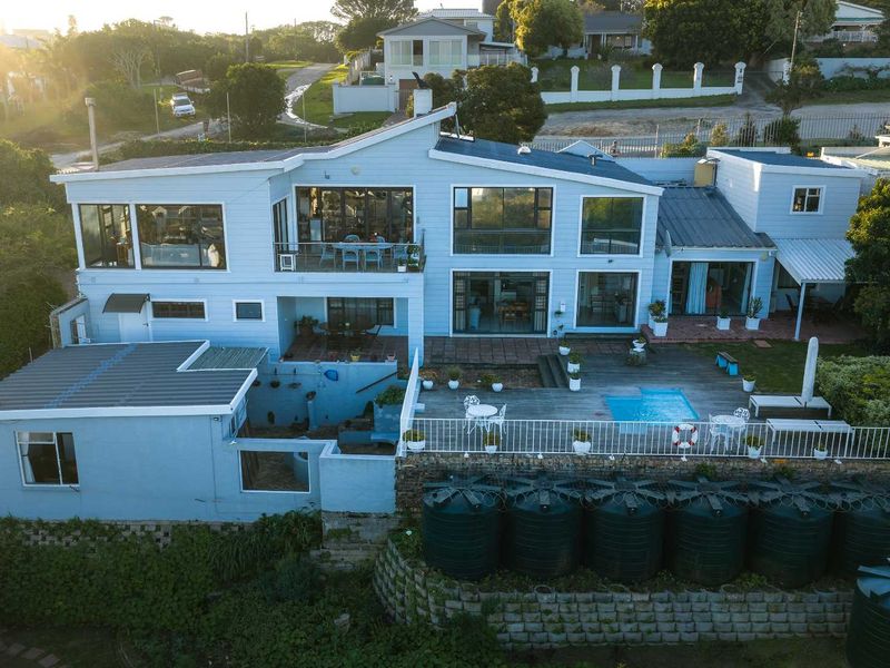 Aerial view of a multi-level residential property featuring a swimming pool, timber deck, and multiple water storage tanks set against a landscaped garden.
