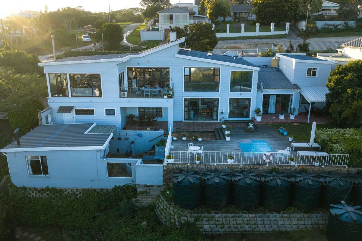 Aerial view of a multi-level residential property featuring a swimming pool, timber deck, and multiple water storage tanks set against a landscaped garden.