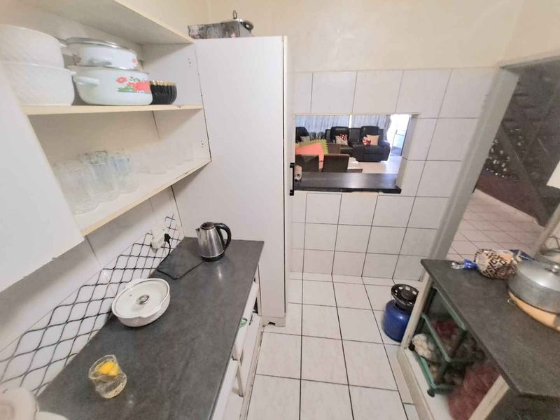 A compact kitchen featuring built-in cabinetry, tiled backsplash, and a convenient pass-through window connecting to the living area.