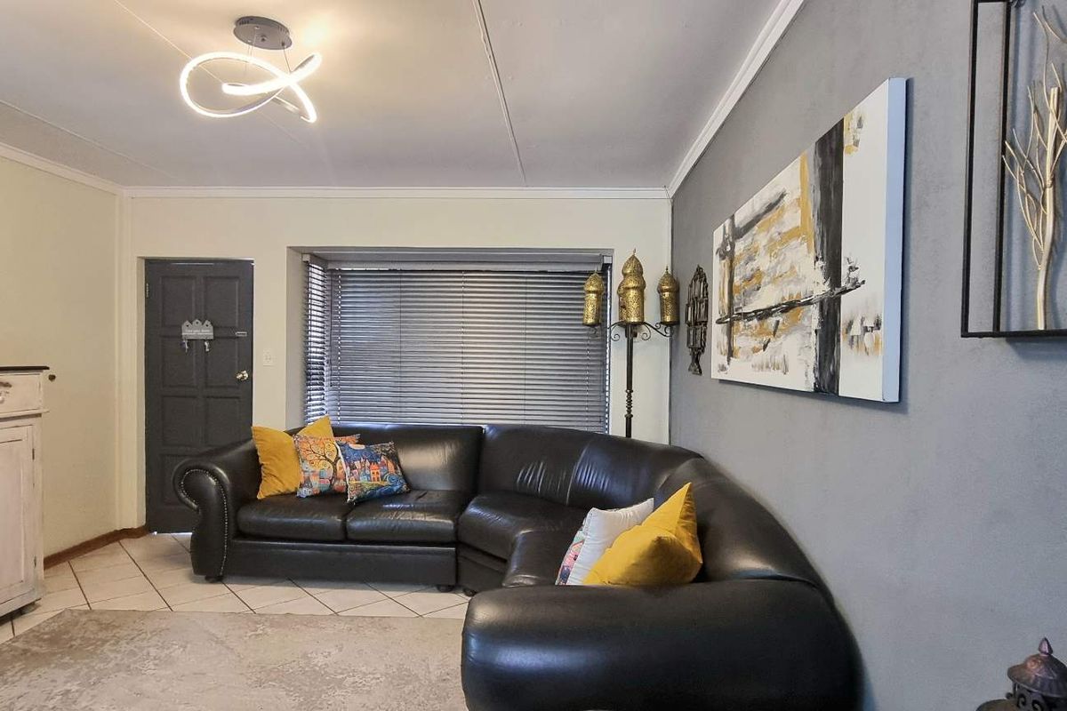 A comfortable living room featuring tiled flooring, a bay window with fitted blinds, and a modern ceiling light fixture.
