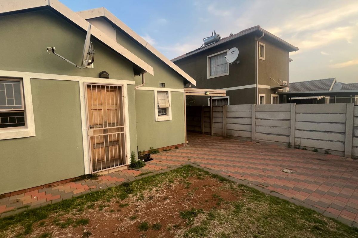 Rear exterior view of the property featuring a paved courtyard, security gate, and precast boundary walling.