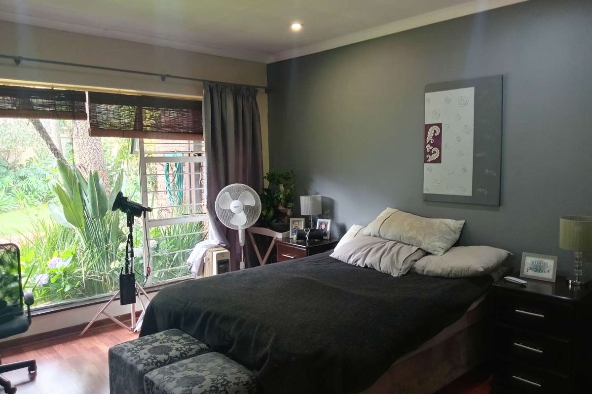 A bedroom featuring dark grey accent walls, laminate flooring, and large windows providing natural light and garden views.