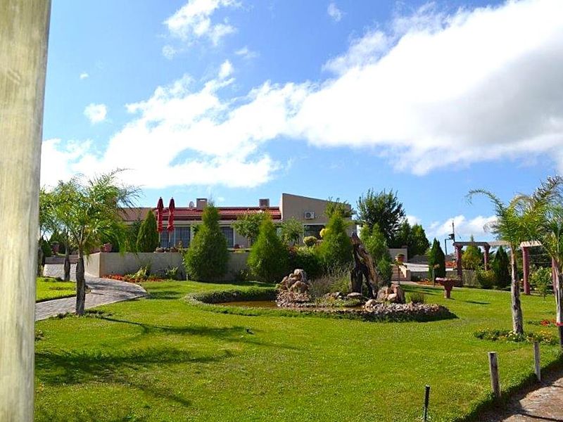 A well-maintained rear garden featuring a landscaped lawn, stone pathways, and a decorative water feature, leading up to the main guest house structure.