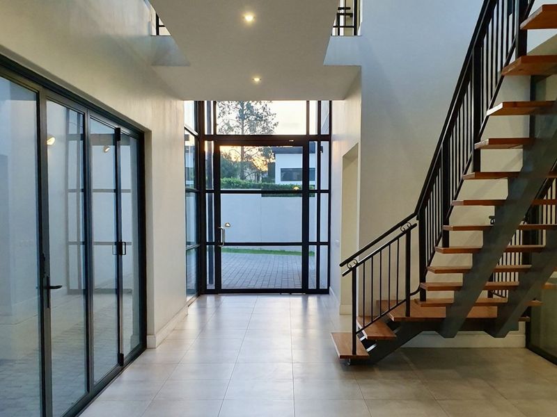 Spacious modern entrance hall featuring a striking open-tread staircase with metal balustrades, large glass doors, and high ceilings with recessed lighting.