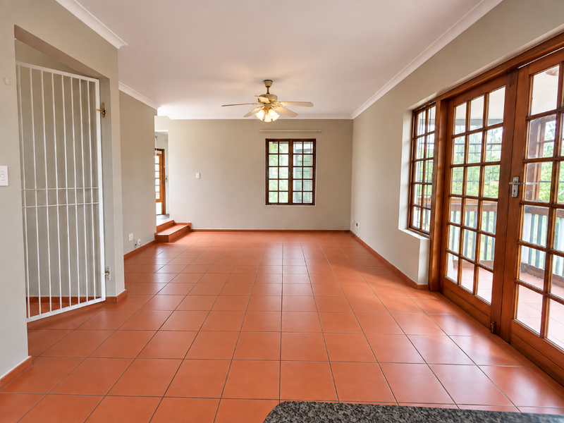 Spacious, empty living area featuring terracotta floor tiles, a ceiling fan, and large wooden-framed glass doors leading to an outdoor space.