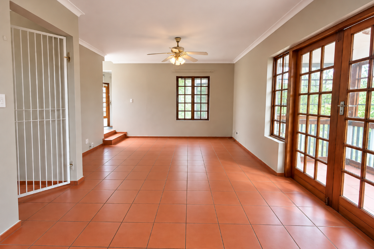 Spacious, empty living area featuring terracotta floor tiles, a ceiling fan, and large wooden-framed glass doors leading to an outdoor space.