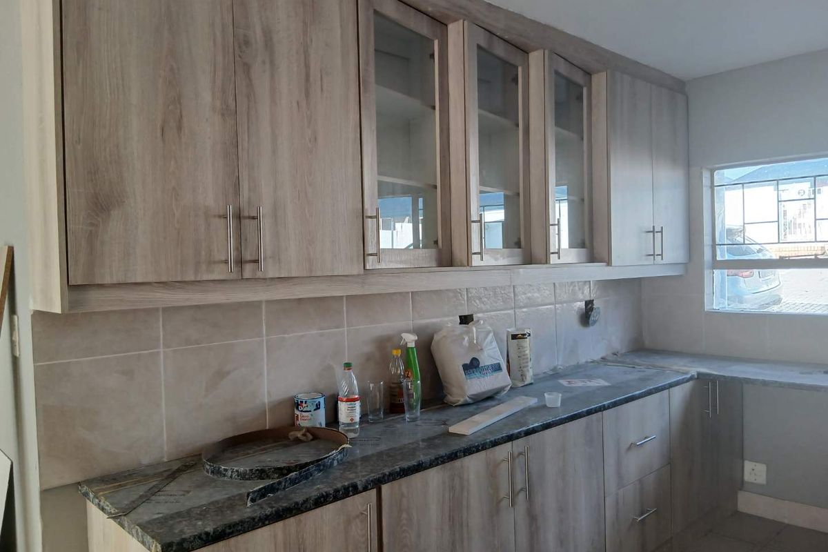 A functional kitchen space featuring light wood-grain cabinetry, glass-fronted upper cupboards, a tiled backsplash, and stone-look countertops, awaiting final finishing touches.