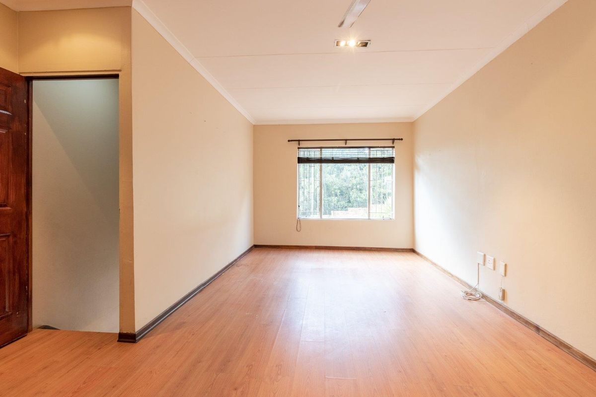 A bright, empty living room featuring laminate flooring, neutral walls, and a window with security bars, offering a clean canvas for personalization.