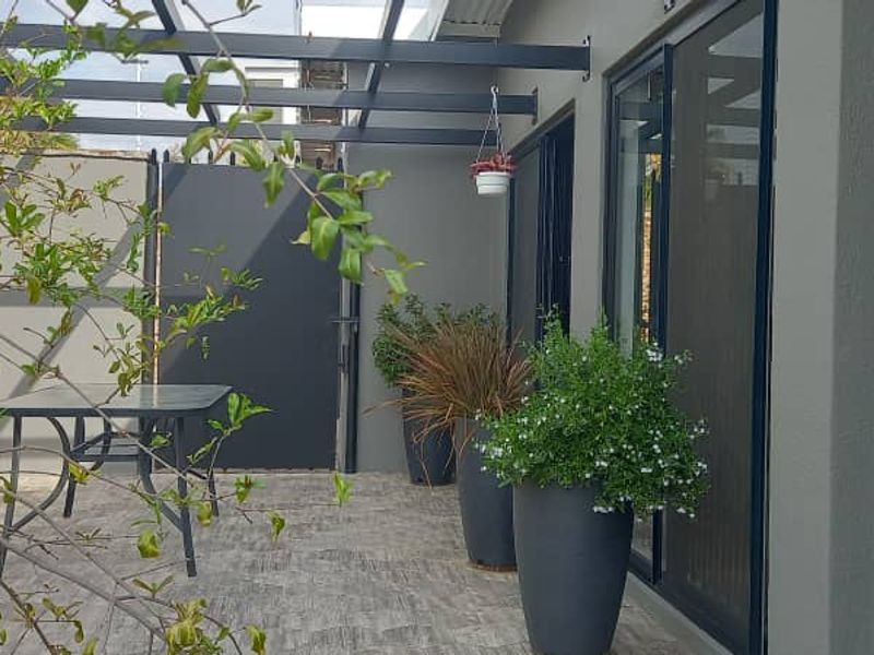 A modern covered patio area featuring a sleek metal pergola, tiled flooring, and sliding glass doors providing seamless access to the home.
