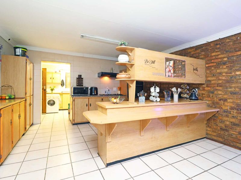 A functional kitchen featuring a breakfast bar, exposed brick wall, and tiled flooring, with an adjacent scullery area visible in the background.