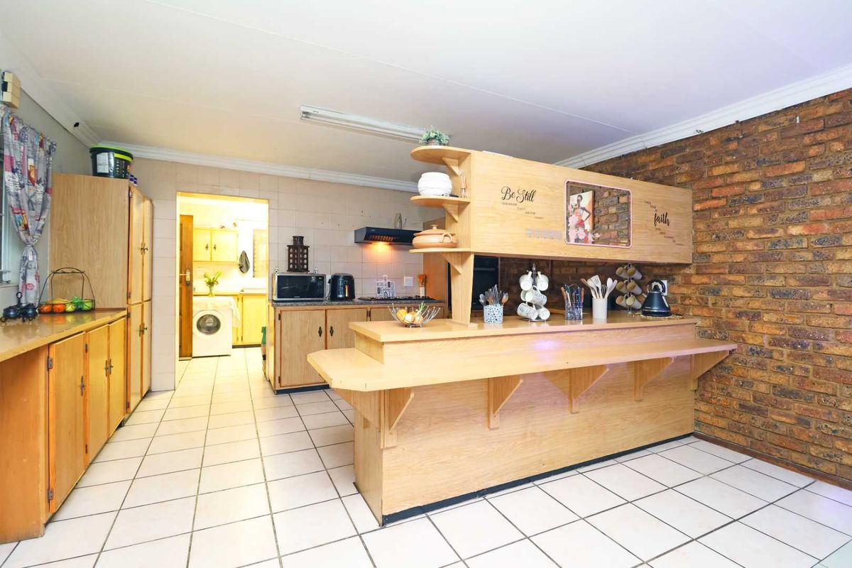 A functional kitchen featuring a breakfast bar, exposed brick wall, and tiled flooring, with an adjacent scullery area visible in the background.