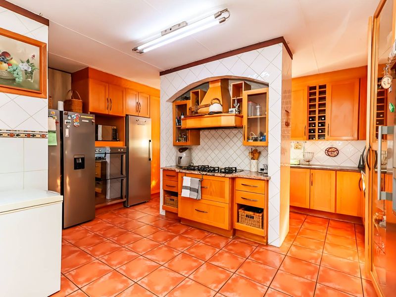 A spacious kitchen featuring extensive wooden cabinetry, a gas hob with extractor fan, tiled backsplash, and terracotta-style floor tiles.