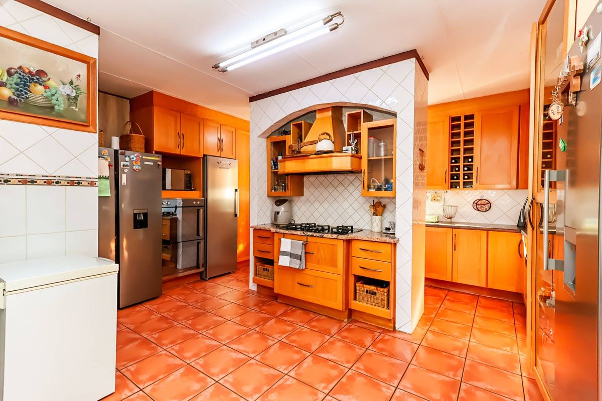A spacious kitchen featuring extensive wooden cabinetry, a gas hob with extractor fan, tiled backsplash, and terracotta-style floor tiles.