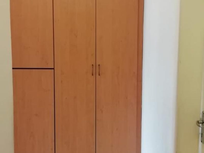 A functional hallway featuring light wood-finish built-in cupboards and neutral tiled flooring.