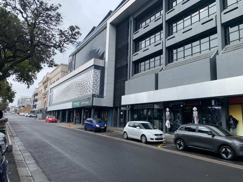 A street-level view of a modern multi-story commercial building featuring a decorative facade, large glass windows, and ground-floor retail shopfronts.