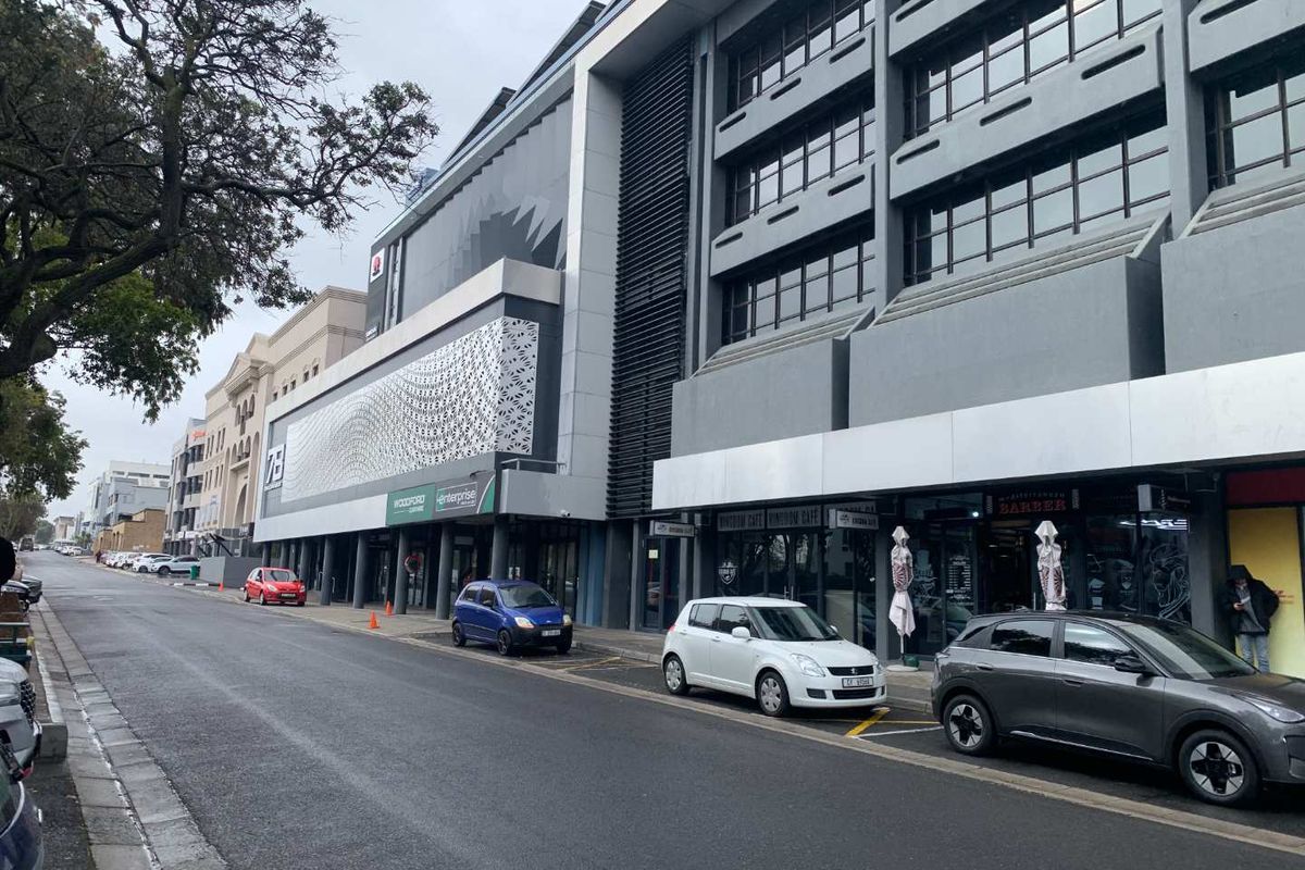 A street-level view of a modern multi-story commercial building featuring a decorative facade, large glass windows, and ground-floor retail shopfronts.