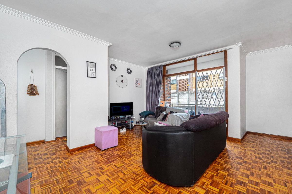 A living room featuring traditional parquet flooring, coved ceilings, and a sliding glass door with a security gate leading to an outdoor area.