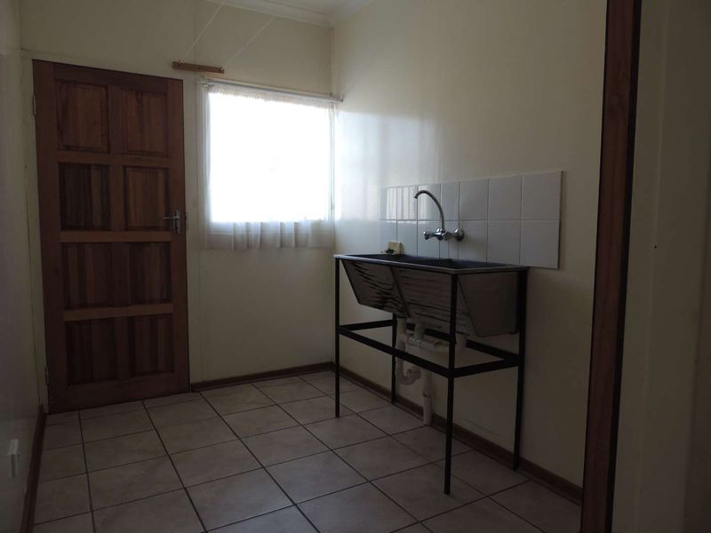 A functional laundry room featuring a stainless steel double sink, tiled splashback, ceramic floor tiles, and a solid timber door.
