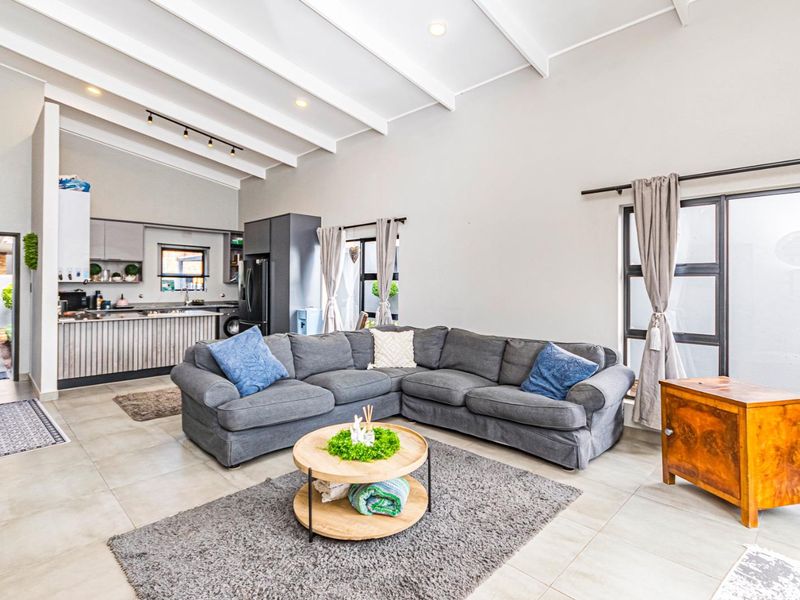 Spacious open-plan living area featuring high exposed beam ceilings, tiled floors, and a modern kitchen, seamlessly connected to outdoor access through large sliding doors.