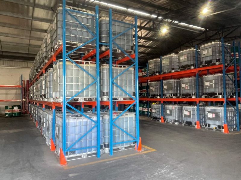 A large industrial warehouse space featuring extensive steel racking systems for bulk storage, concrete flooring, and high-clearance exposed roof structure.