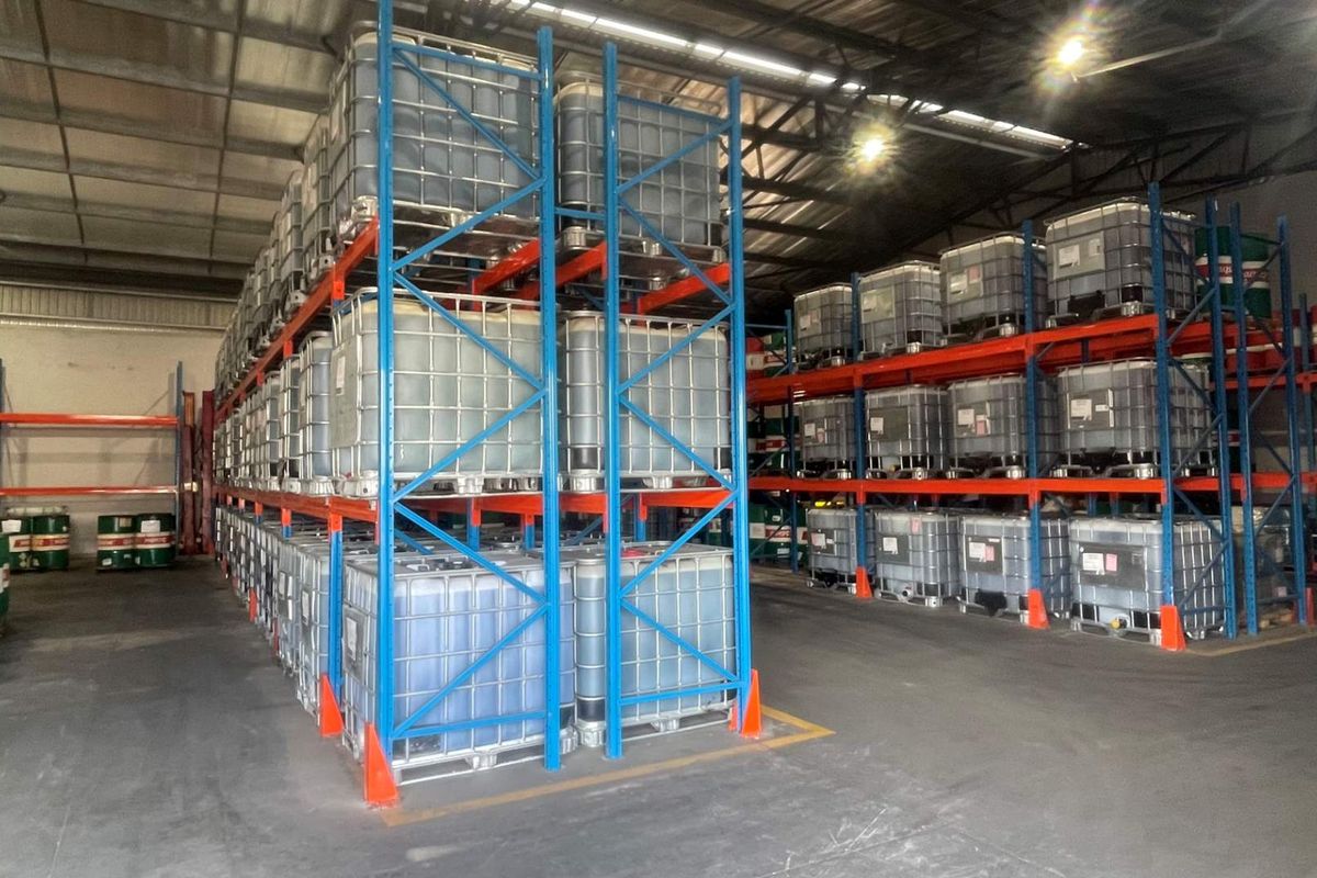 A large industrial warehouse space featuring extensive steel racking systems for bulk storage, concrete flooring, and high-clearance exposed roof structure.