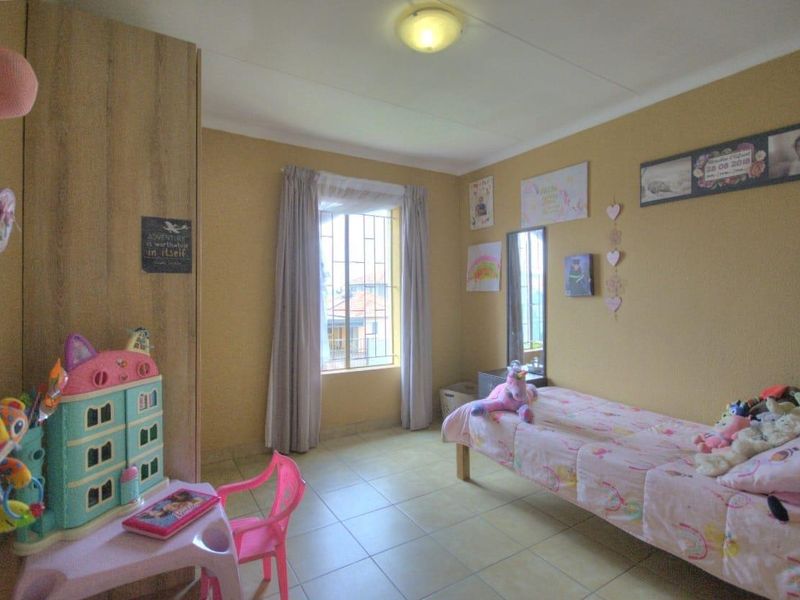 A functional bedroom featuring tiled flooring, a built-in wardrobe, and a window fitted with security bars.