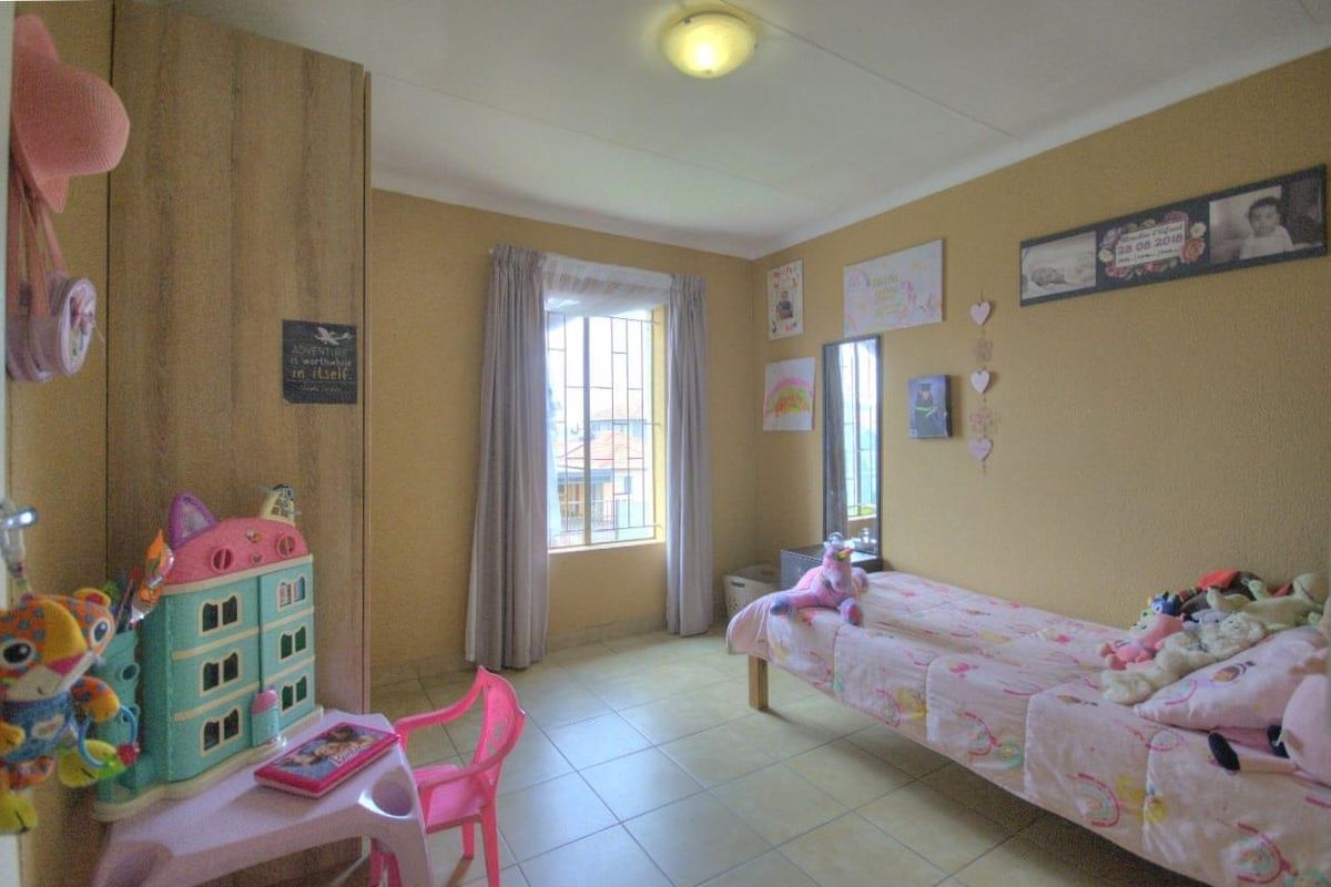 A functional bedroom featuring tiled flooring, a built-in wardrobe, and a window fitted with security bars.