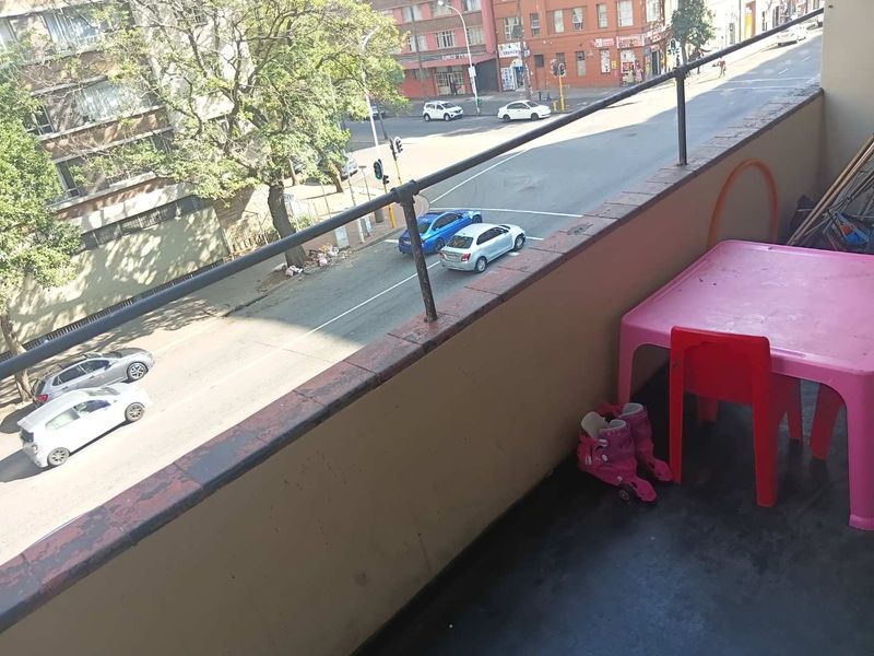 An open balcony area featuring a metal safety railing and tiled flooring, overlooking a busy urban street.