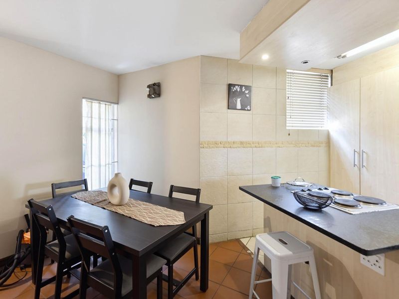 Open-plan kitchen and dining area featuring tiled flooring, built-in cabinetry, and a breakfast bar with an integrated electric hob.