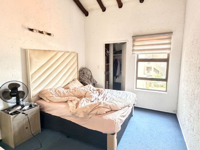 Bedroom featuring high vaulted ceilings with exposed timber beams, a built-in closet, and a window with a roller blind.