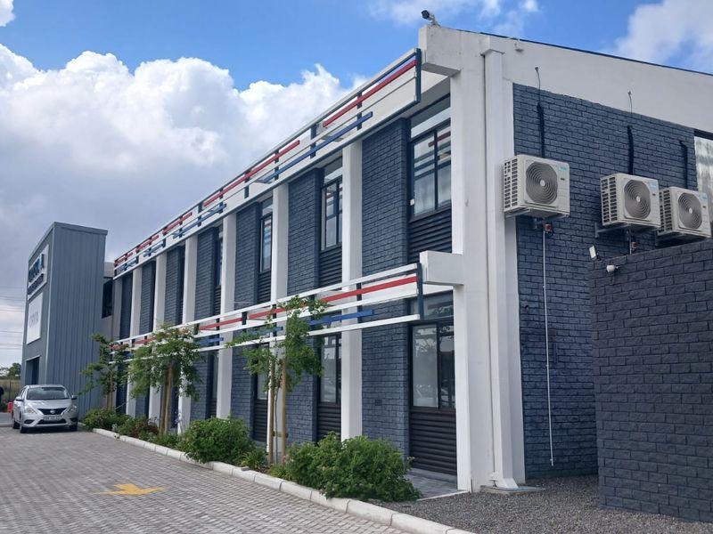Modern office building exterior featuring a dark brick facade, decorative trim, and integrated external air conditioning units with adjacent paved parking.