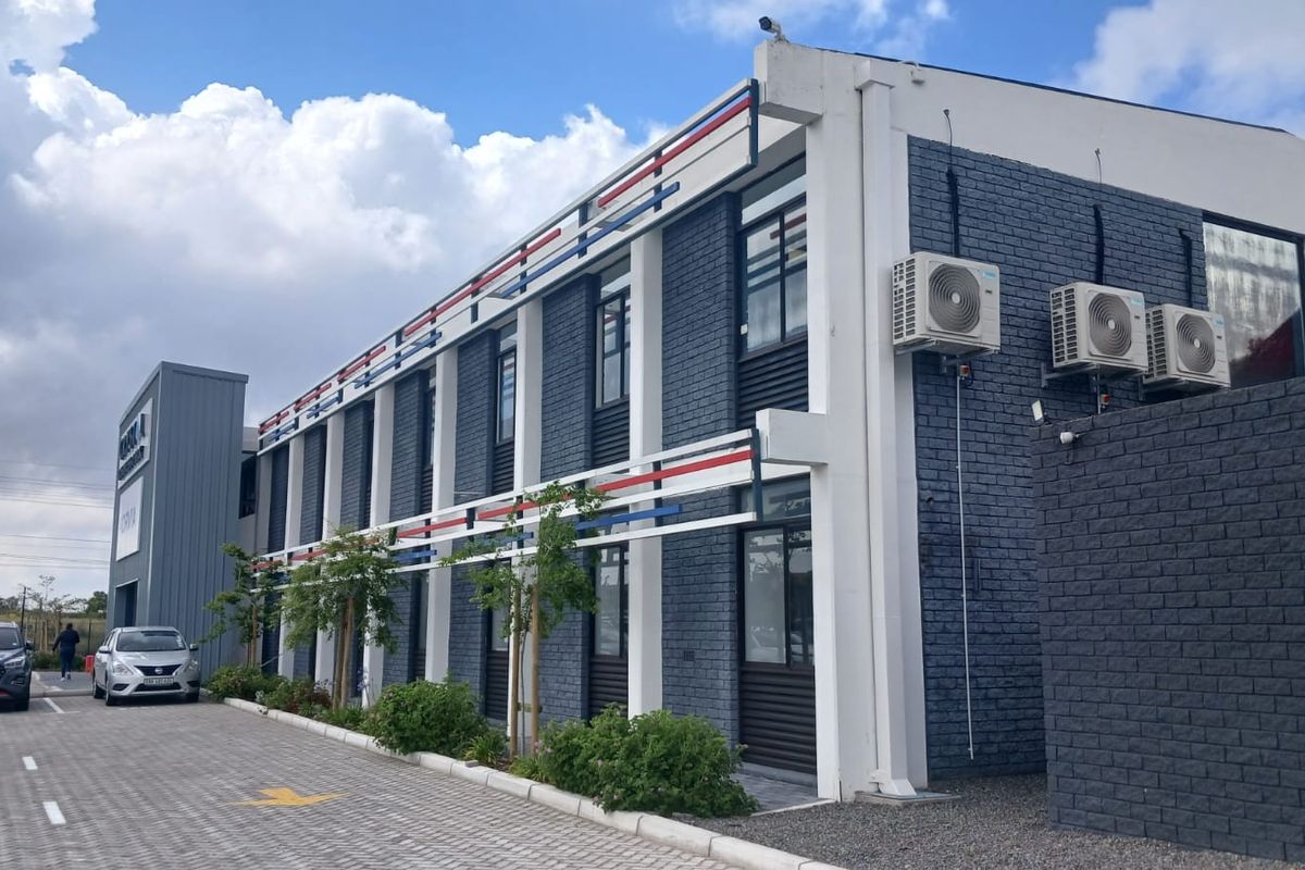 Modern office building exterior featuring a dark brick facade, decorative trim, and integrated external air conditioning units with adjacent paved parking.