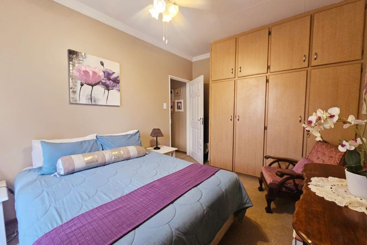 A well-maintained bedroom featuring built-in wooden cupboards, crown molding, and a ceiling fan, offering a comfortable and functional living space.