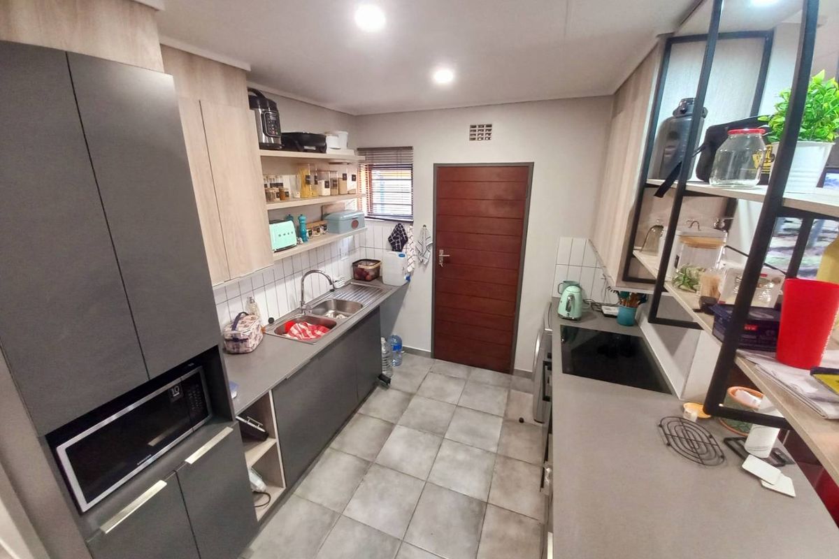 A modern galley-style kitchen featuring dark grey cabinetry, light wood-tone accents, integrated oven, induction hob, and tiled flooring.