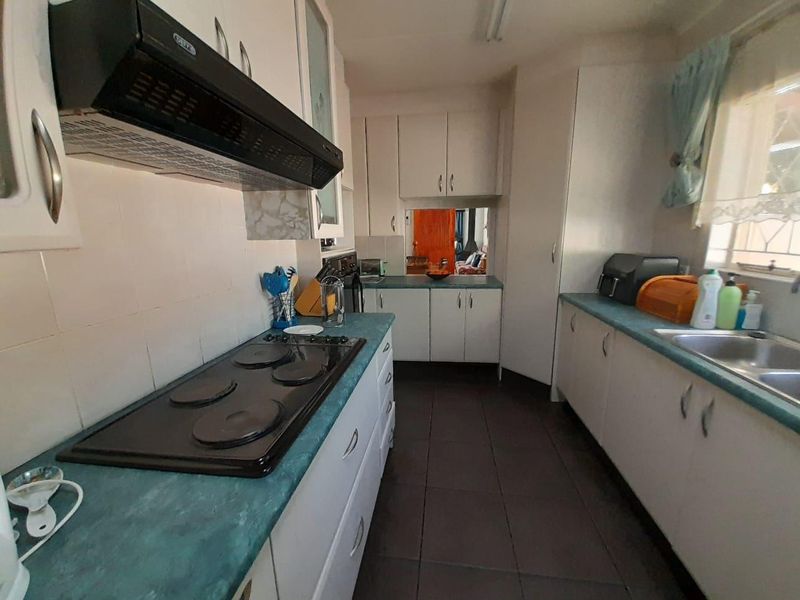 A functional kitchen featuring white cabinetry, laminate countertops, a built-in electric hob with extractor fan, and tiled flooring.