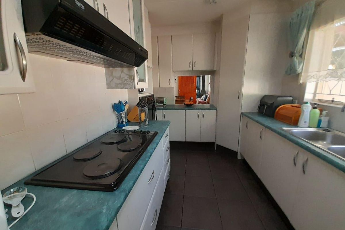 A functional kitchen featuring white cabinetry, laminate countertops, a built-in electric hob with extractor fan, and tiled flooring.