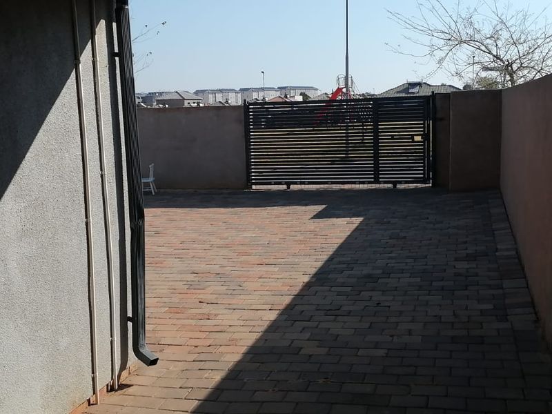 A paved rear courtyard area featuring a secure metal sliding gate and perimeter boundary walls.
