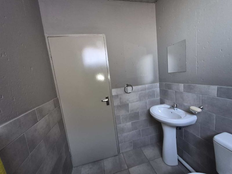 A functional bathroom featuring a pedestal basin, tiled flooring, and wall tiling, providing a clean and neutral space.