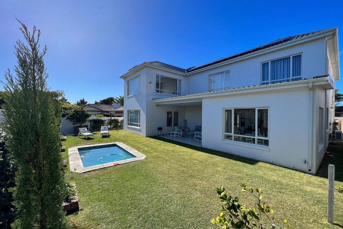 Rear view of the property featuring a well-maintained lawn, a swimming pool, and a covered patio area attached to the main house structure.