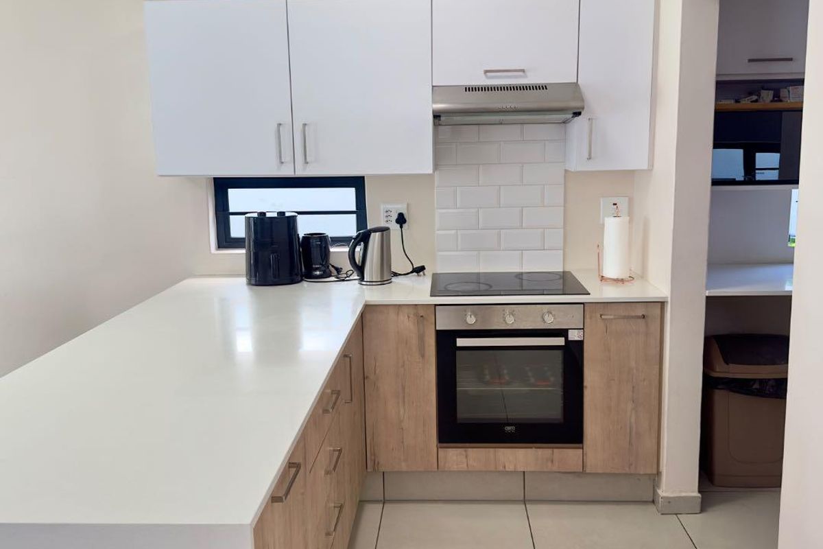 Modern kitchen featuring light wood-finish cabinetry, white stone countertops, subway tile backsplash, and integrated electric cooking appliances with an adjacent scullery area.