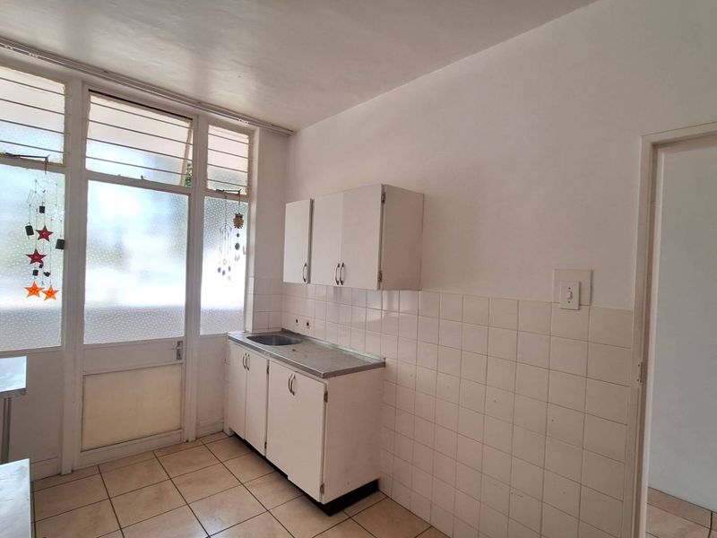 A compact, empty kitchen featuring basic built-in cabinetry, a stainless steel sink, tiled splashbacks, and tiled flooring with access to an exterior door.