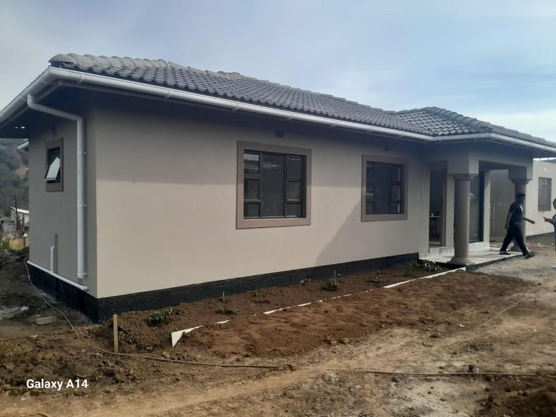 A modern single-story house exterior featuring a tiled roof, plastered walls, and concrete columns, currently undergoing final landscaping works.